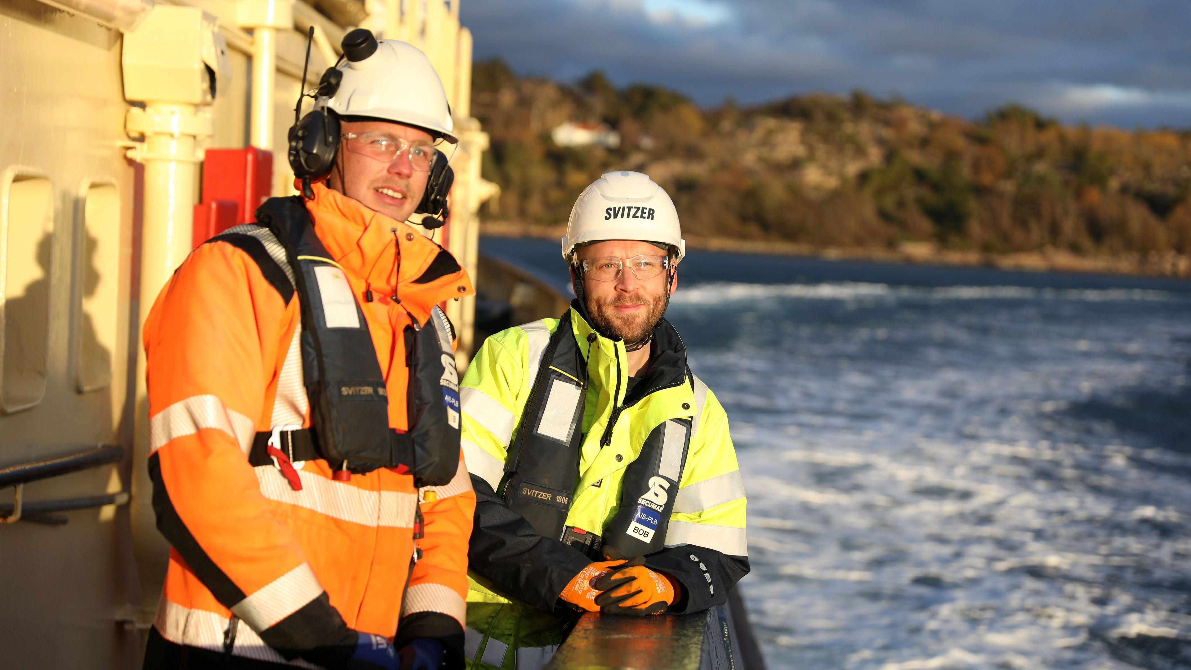 Två matroser ombord en bogserbord står i solen med havet vid sidan av
