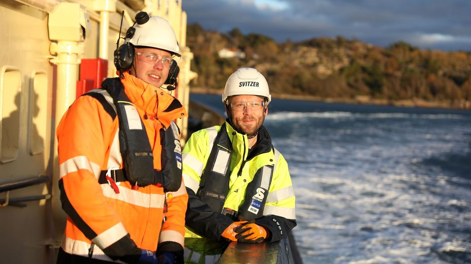 Två matroser ombord en bogserbord står i solen med havet vid sidan av