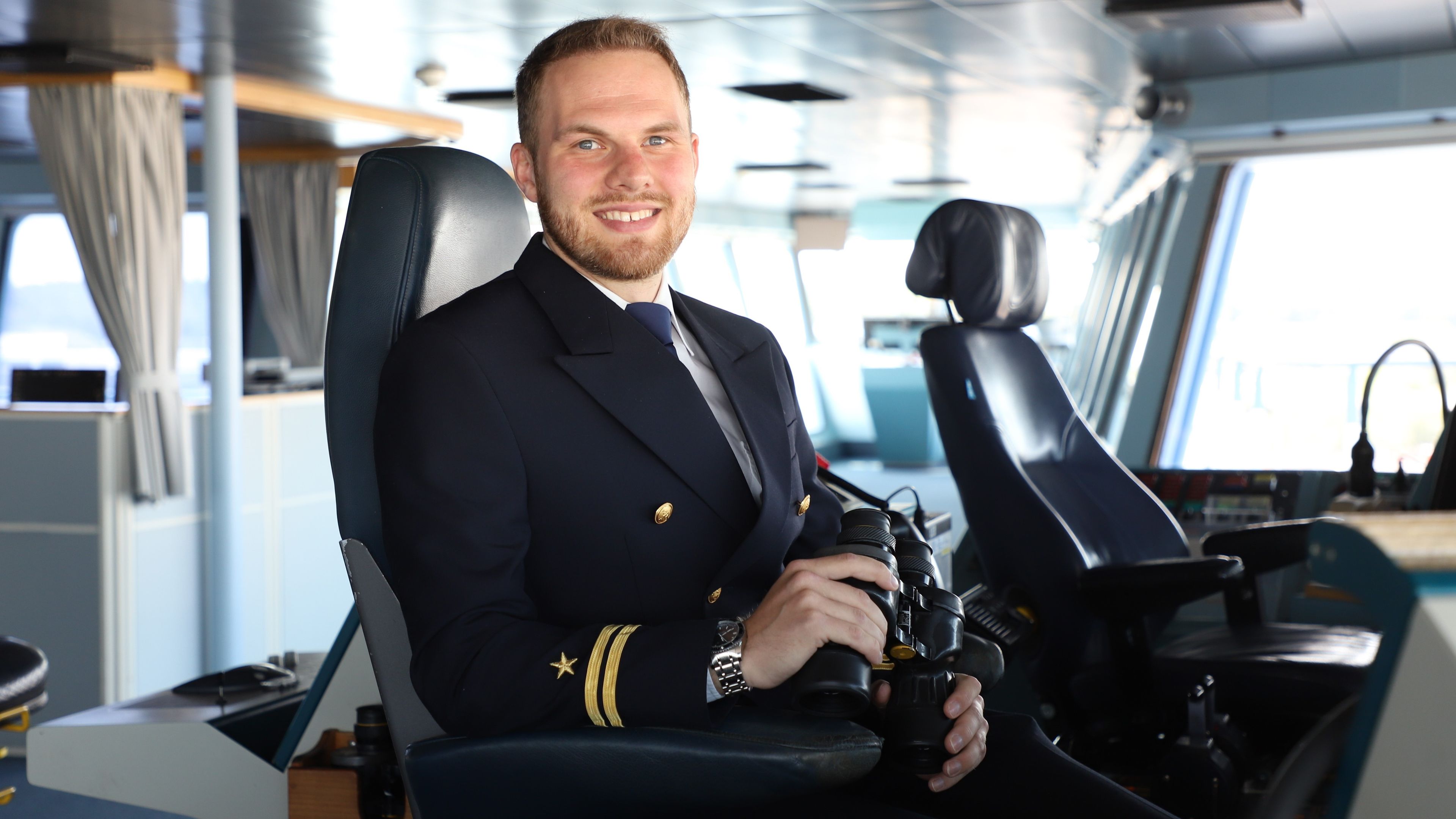 En leende andrestyrman sittandes på en fartygsbrygga ombord. 