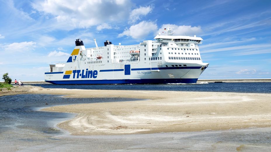 Ett av TT-lines fartyg till sjöss med strand i förgrunden.