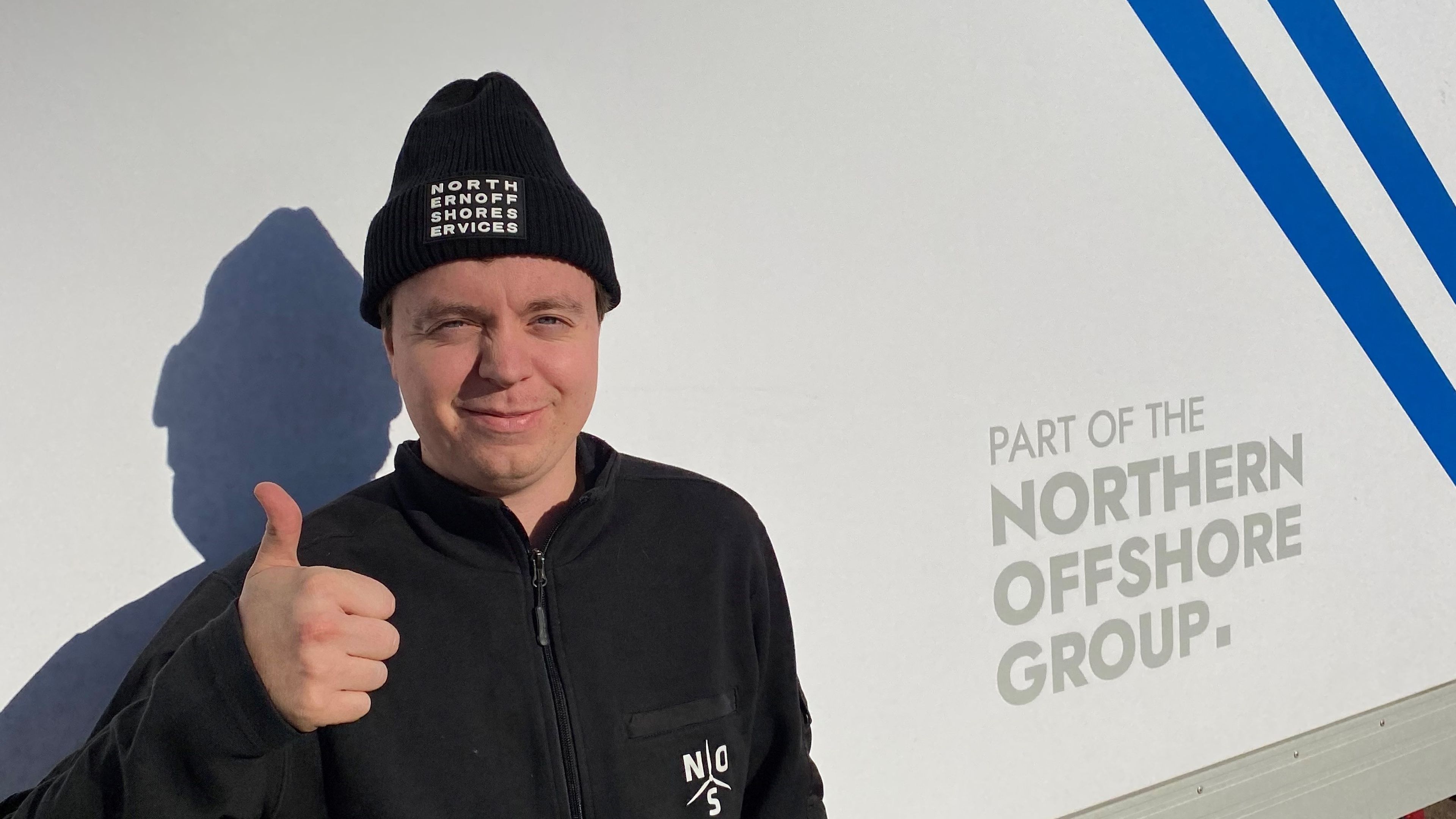 Matrosen Peter står framför ett servicefartyg och ger tummen upp mot kameran. 